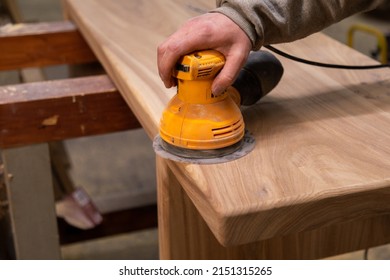 Closeup of carpenter sanding wood table with orbital sander in a workshop