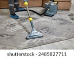Close-up of carpet cleaning by a professional worker in overalls and shoe covers with a vacuum cleaner in a spacious living room.