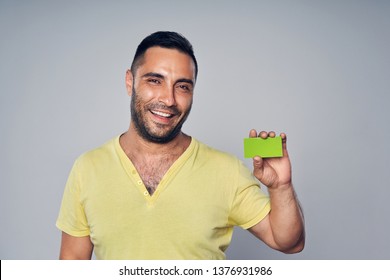 Closeup Of Casual Hispanic Man Looking At Camera And Showing Blank Credit Card, Studio Portrait Over Gray Background