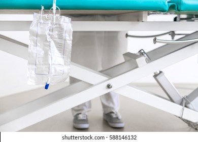 closeup of an catheter bag on an hospital bed, in the background the legs of an nurse or doctor