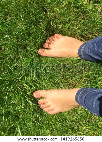 Closeup of Caucasian bate feet with unpainted toe nails with blue Jean leggings in grass