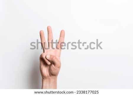 A close-up of a Caucasian male hand shows gesture number three isolated on a white studio background.