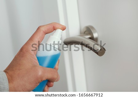 closeup of a caucasian man disinfecting the door handle by spraying a blue sanitizer from a bottle