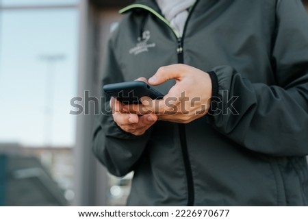 Close-up of caucasian man in jacket using mobile phone, chatting in smartphone outdoors.