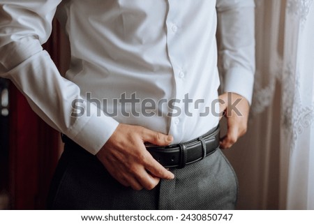 closeup of caucasian man putting on his belt. A stylish man puts on a leather belt close-up. Fashion