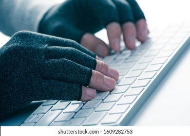 closeup of a caucasian man wearing a pair of compression gloves while is typing on a computer keyboard