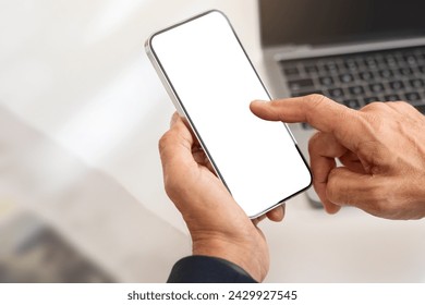 Close-up of a caucasian man's hands using a smartphone with a blank screen, with the keyboard of a laptop in the background, illustrating connectivity and technology use, cropped - Powered by Shutterstock