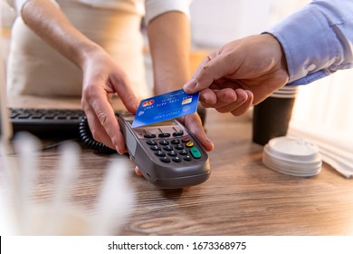 Closeup Of Caucasian Man's Right Hand, Holding Blue Credit Card On A PIN PAD Held By A Woman's Hands