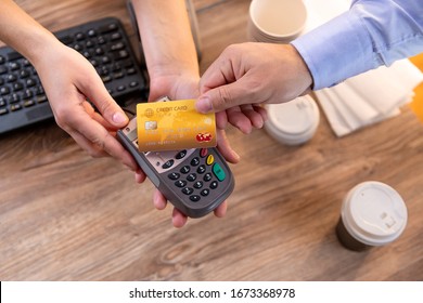 Closeup Of Caucasian Man's Right Hand, Holding Gold Credit Card On A PIN PAD Held By A Woman's Hands