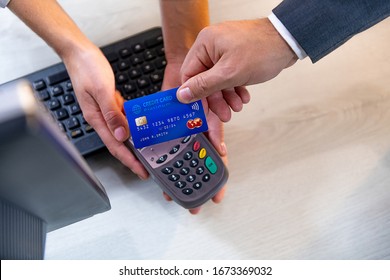 Closeup Of Caucasian Right Hand, Holding Blue Credit Card On A PIN PAD Held By A Woman's Hands