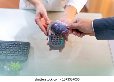 Closeup Of Caucasian Right Hand, Holding Blue Credit Card On A PIN PAD Held By A Woman's Hands