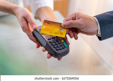 Closeup Of Caucasian Right Hand, Holding Gold Credit Card On A PIN PAD Held By A Woman's Hands