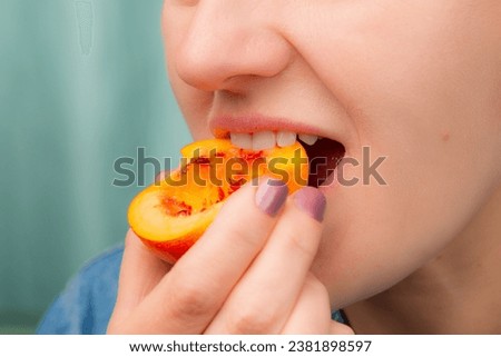 Close-up of a Caucasian woman eating a slice of fresh peach.