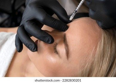 Closeup of Caucasian woman gets botulinum toxin cosmetic injection in forehead. Beauty physician inserts needle of syringe into between the eyebrows, face of female. Cosmetologist, aesthetic medicine. - Shutterstock ID 2282830201