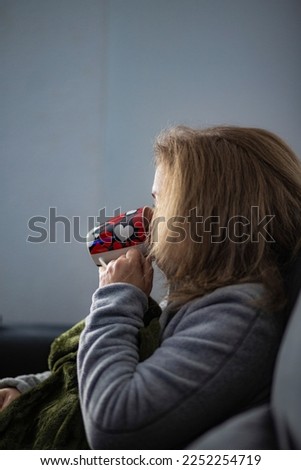 Close-up of a caucasian woman in a green plaid drinking hot coffee on the sofa at home. Cozy, comfortable, winter, autumn, break and relax concept.