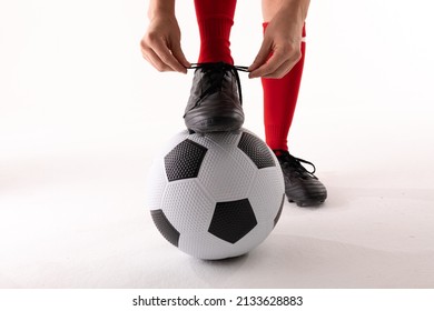 Close-up Of Caucasian Young Female Player Tying Soccer Shoe Lace While Standing With Foot On Ball. White Background, Unaltered, Sport, Soccer Shoe, Sock, Athlete And Women's Soccer.