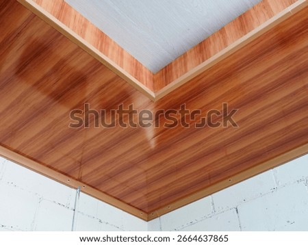 A close-up of a ceiling installation using modern PVC panels with a wood-grain texture, highlighting the clean, modern look of the material.