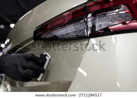 Close-up of ceramic coating being applied to a rear car body panel near the taillight by a gloved detailer, showing precise work, paint protection and premium car detailing process.