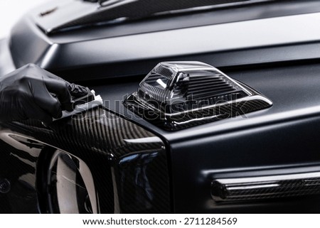 Close-up of ceramic coating being applied to a carbon fiber exterior element on a luxury car, highlighting precision work, surface protection, deep gloss and premium car detailing service.