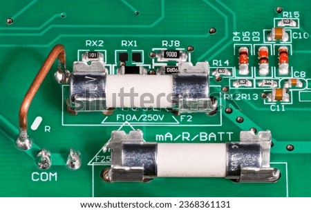 Closeup of ceramic tubes of electrical fuses in metal holder on circuit board. Low ohm wire resistor to current measuring, capacitors or red diodes. Surface mounted electronic components on green PCB.