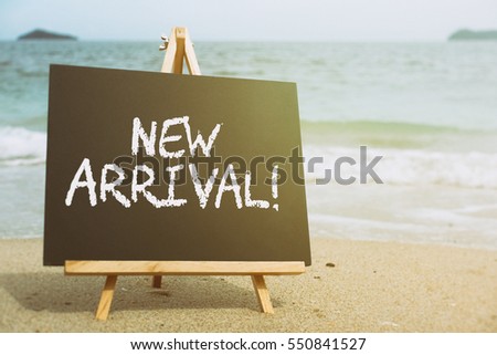 Closeup chalkboard on the beach with text NEW ARRIVAL!. Retro filtered, conceptual image.