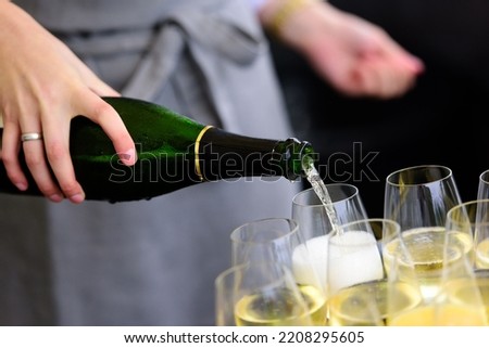 closeup of a champagne bottle pooring champagne into a champagne flute against a blurred person at a party