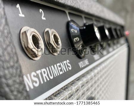 Close-up channel 2 input jack of vintage combo amplifier with blurred knob, speaker grill cloth, and control panel on grey polished cement background, Music business concept.
