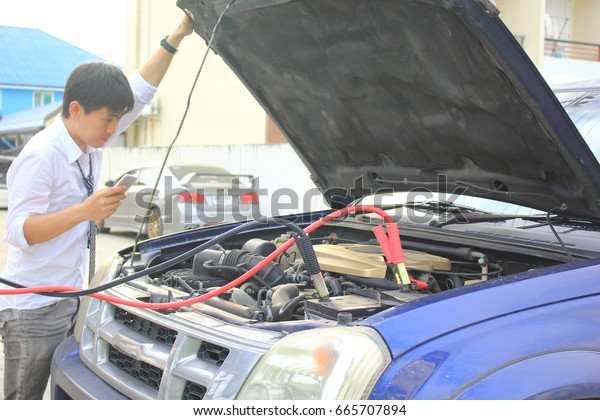 Close-Up Of Charging automobile\
discharged battery and Man calling to car mechanic\
service
