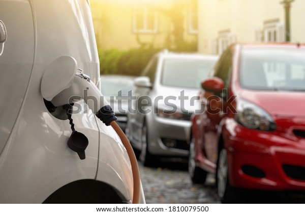 Close-up of a charging electric car on the\
background of parked\
cars