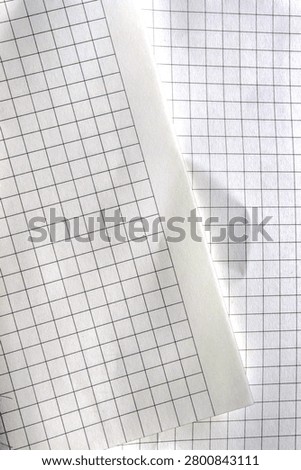 Close-up of checkered notebook paper texture with a subtle crease and shadows.