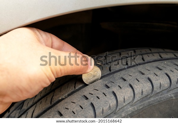 Closeup of checking tire tread wear depth of old\
tire using a quarter coin. Concept of automobile safety,\
maintenance and repair