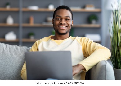 Closeup Of Cheerful Black Guy Using Laptop At Home, Copy Space. Handsome African American Young Man Sitting On Couch And Chatting Online, Male Freelancer Working From Home, Smiling At Camera