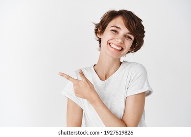 Close-up Of Cheerful Candid Woman Tilt Head Cute And Pointing Left, Showing Logo Or Advertisement, Wearing White T-shirt.