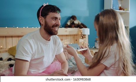 Close-up cheerful daughter doing lovely make-up to her father. Little girl dresses her smiling dad like fairy having cool costume party at home. - Powered by Shutterstock