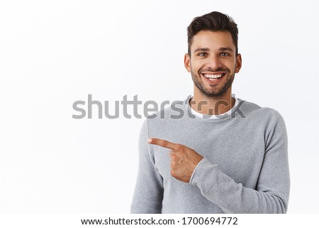 Close-up cheerful good-looking outgoing bearded modern man in grey sweater asking out for coffee, pointing left and smiling, inviting check out see new promo, recommend corporate banner