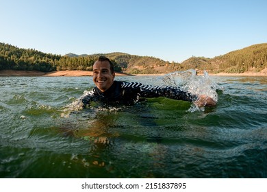 Close-up Of Cheerful Smiling Wet Man In A Black Wetsuit Floats On The River Water. Summertime Watersports Activity