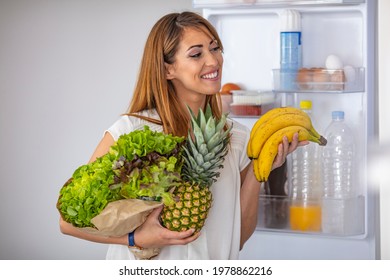 Closeup Of A Cheerful Young Couple Picking Some Fruit And Veggies From The Fridge To Make Some Healthy Breakfast On Sunday Morning. A Side-view Shot Of A Woman Taking Something Out Of The Fridge.