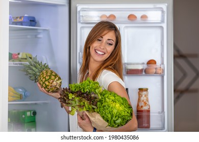 Closeup Of A Cheerful Young Couple Picking Some Fruit And Veggies From The Fridge To Make Some Healthy Breakfast On Sunday Morning. A Side-view Shot Of A Mature Caucasian Woman Taking Something 