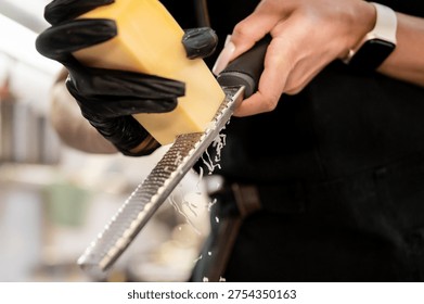 Close-up of a chef in black gloves using a professional stainless steel microplane to grate hard cheese, with fine shavings falling against a dark background.