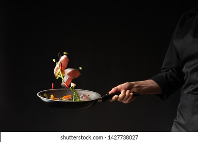 Close-up. Chef cook fry fish with vegetables on a griddle on a black background. horizontal photo. sea food. healthy food. oriental cuisine, baner