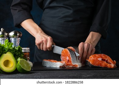 Close-up of chef cuts with knife the salmon at the professional kitchen. Dark background for background. Backstage of preparing restaurant dinner. Food concept.