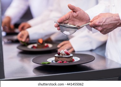 Close-up of chef finishing a dessert plate with icing sugar in the kitchen - Powered by Shutterstock