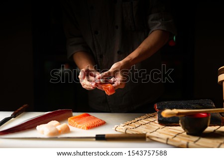 Closeup of chef hands preparing japanese food. Japanese chef making sushi at restaurant. Young chef making traditional japanese sushi on cuting board .