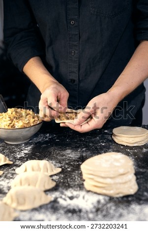 Close-up of chef hands stuffing wrappers with minced meat, cooking traditional Asian gyoza or dumpling on the black table.