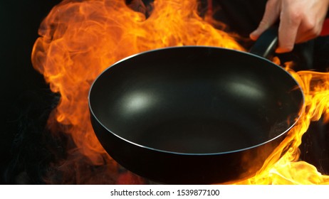 Closeup Of Chef Holding Empty Wok Pan With Flames. Isolated On Black Background