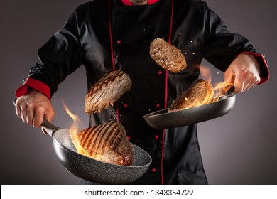 Closeup Of Chef Throwing Beef Steaks Into The Air, Fire Flames Around. Concept Of Food Preparation