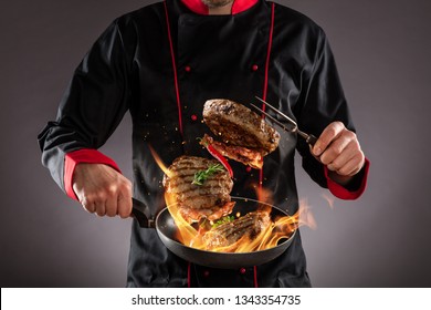 Closeup Of Chef Throwing Beef Steaks Into The Air, Fire Flames Around. Concept Of Food Preparation