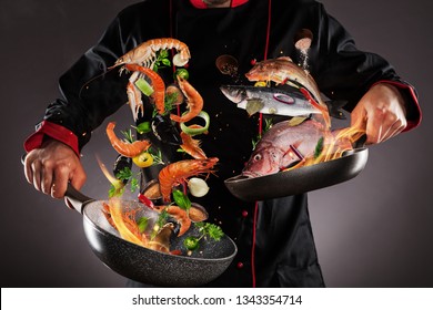 Closeup Of Chef Throwing Sea Fruit And Fish Into The Air, Fire Flames Around. Concept Of Food Preparation