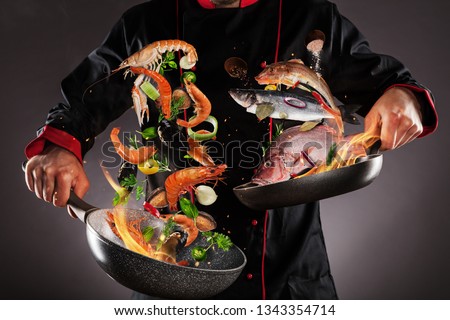 Closeup of chef throwing sea fruit and fish into the air, fire flames around. Concept of food preparation