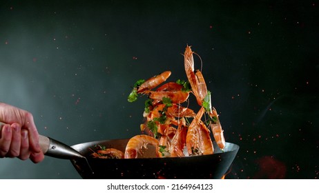 Closeup Of Chef Throwing Shrimps From Wok Pan In Fire. Fresh Asian Food Preparation On Dark Background.